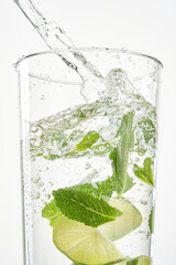 Clear shiny glass filled with lime and mint and delicious Mojito cocktail composed. Stream of water into a glass on white background.  Shallow depth of field