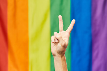 Closeup of hand showing V sign against rainbow flag in background for Pride month