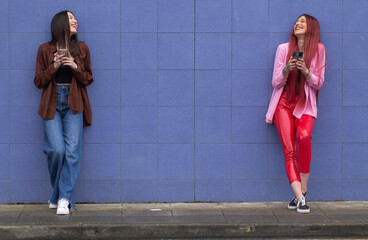 young female friends with mobile phone on blue wall