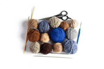 Fototapeta na wymiar Blue, gray and brown balls of knitting thread with scissors, crochet and knitting needles on a blue background for hobbies. Flat lay
