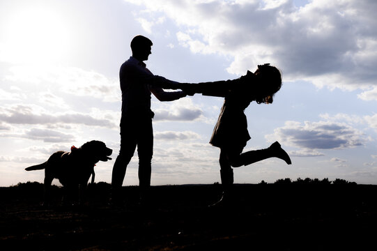 Silhouette of a loving couple with a Labrador dog on a background of sky and fields