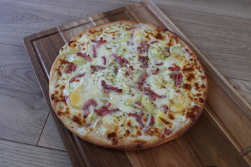 Pizza tartiflette sur plateau en bois, lardons, pommes de terre, oignons, reblochon