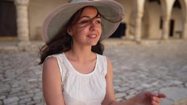 Portrait of young beautiful woman laughing sitting outdoors looking away on vacations. Happy carefree Caucasian tourist in straw hat enjoying summer day on Cyprus smiling