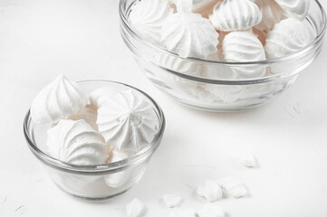 two glass vases different sizes with French meringue dessert on gray background, broken pieces of meringue lie next each other. large vase with meringue stands in background and ipartially visible.