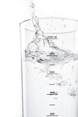 Pouring water into glass on white background. Stream of water into a glass beaker with measure....