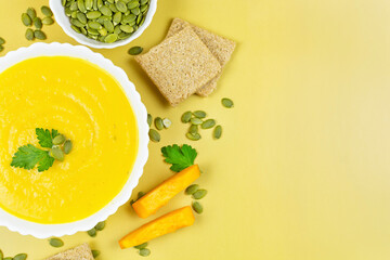 Pumpkin soup puree in a white bowl with parsley, pumpkin seeds and slices, crusty bread close-up on...
