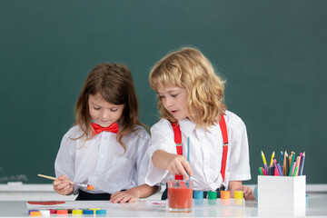 Funny pupils draws in classroom on school blackboard background. School friends kids boy and girl painting together in class. Little artists painting, kids drawing art.
