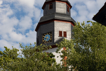 Close up church tower with clock. Ancient clock with blue and golden shiny clock-face. Sunny day with blue sky and few clouds.