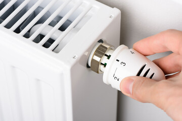 Hand adjusting the valve knob of heating radiator temperature thermostat in winter cold season