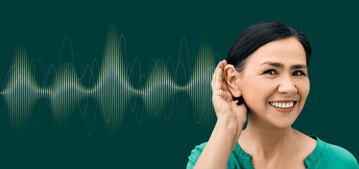 Positive woman with hand near ear and with luminous sound wave on green background showing variety...