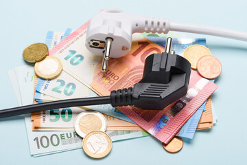 Two european electric power plugs on Euro banknotes and coins on blue background. Concept of...