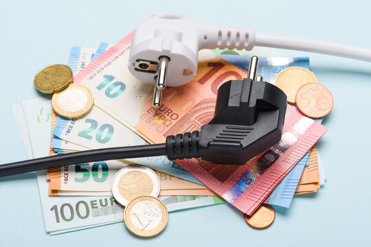 Two european electric power plugs on Euro banknotes and coins on blue background. Concept of expensive electricity costs and rise in energy bill prices.