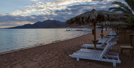 Dahab, Egypt - January 2022: View of the beach with umbrellas and chaise-longues in the evening - obrazy, fototapety, plakaty