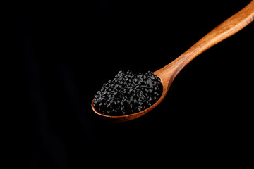 Wooden spoon with black caviar isolated on black background.