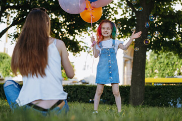 Mother and daughter having fun in park blowing bubbles. Girl holding baloons for birthday