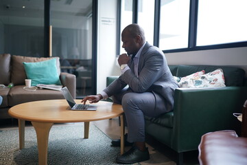 Portrai of African American businessman using  laptop of mobile device  in modern office.