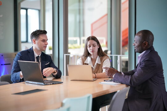 Image of young businessmen and colleague discussing document in laptop and touchpad at meeting