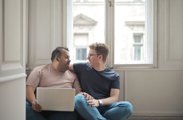 homosexual couple sitting on the floor in the house with a laptop - 508215396