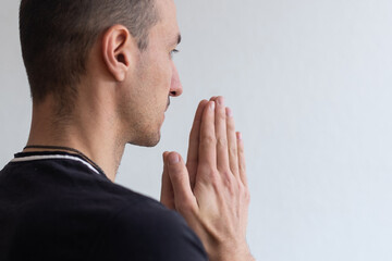 Naklejka premium Man praying. Concentrated young man in white shirt holding hands clasped near face while standing against grey background