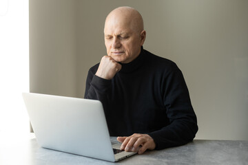 Handsome old man dressed in smart casual style is using a laptop