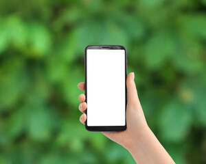 Hand with the phone upright against blurred greens. Smartphone with a white screen, copy space.