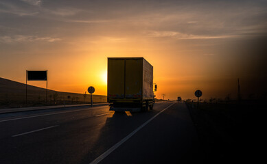 Truck traveling on asphalt road in rural landscape at sunrise