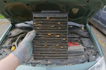 Auto mechanic in gloves holds an old dirty clogged car air filter. Car engine repair and...