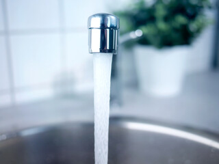A stream of clean water drink flows from the kitchen faucet into the stainless steel sink....