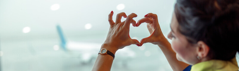 Close up of woman stewardess making heart sign with hands while looking out the window in airport...