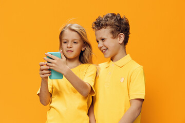 cute, funny children, school age, brother and sister stand on a yellow background and look into their smartphone