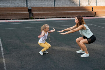 Fototapeta na wymiar Mother and daughter go in for sports outdoors. Caucasian woman and little girl are engaged in fitness at the stadium.