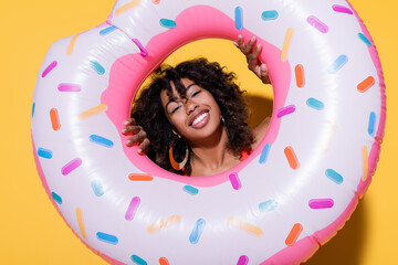 brunette african american woman smiling at camera through swim ring on yellow background.