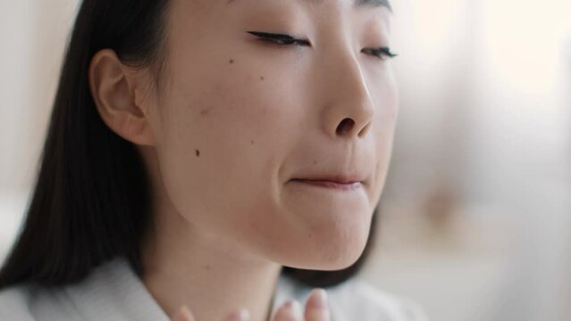 Lips care. Young pretty asian lady applying pampering balm on lips with finger at home, slow motion, empty space