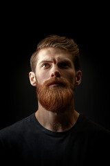 Fototapeta premium Attractive brutal young bearded man raised his head and looked up. Bearded man closeup portrait