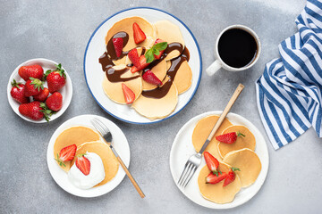 Pancakes served with fresh strawberries, chocolate syrup and yogurt, concrete table background. Top view. Family breakfast concept