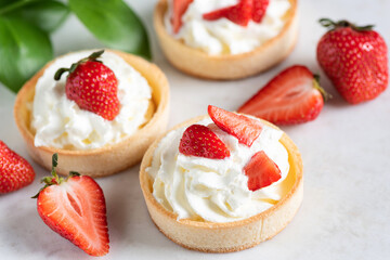 Shortcrust mini tarts with whipped cream and strawberries, closeup view