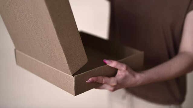 female hands with pink manicure open a cardboard empty box close-up. Inviting camera focus