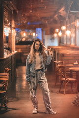 A woman stands inside an evening deserted luminous cafe with a wooden interior. Soft focus.