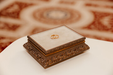 two gold wedding rings lie on a carved ring cushion decorated with beige velvet