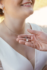 a man holds a pendant made of white gold and pearls, put on a smiling bride