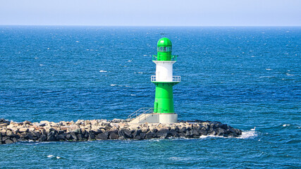 Fototapeta na wymiar green white lighthouse on the Warnow River in Rostock on the Baltic Sea. Waves on the stone edge.