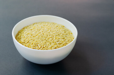 Raw risoni pasta in a white bowl on a dark background. The concept of vegetarian cuisine. Risoni is suitable for making salads. Horizontal orientation.