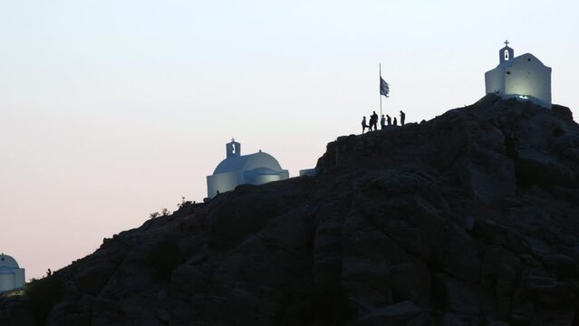 Tourists exploring the picturesque small chapels up the hill in Ios Greece while the sun is setting