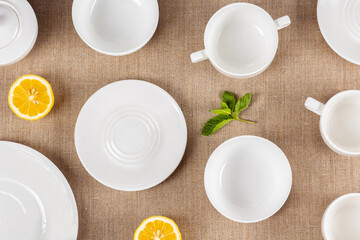 Fototapeta na wymiar Set of white dishes on coarse linen cloth with halved lemons and fresh mint leaves