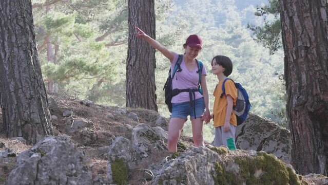 A woman walks with her son through the forest, The boy with his mother go hiking, A child with a backpack is in the park, Travel with children, The kid holds mom's hand, Mountain trail, Mothers Day.