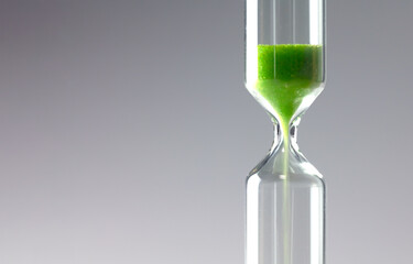 Diminishing green. Ecology / environment concept image. Green sand of hour glass or sand clock falling down.