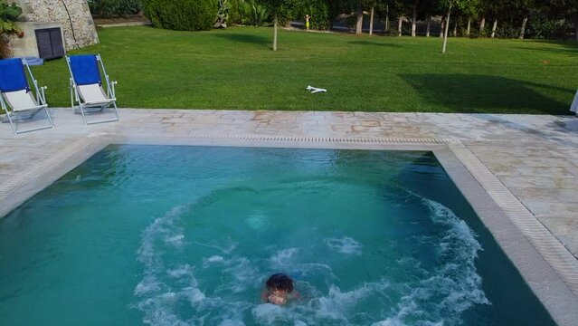 Boy child jumping into a pool with blue water. Leisure activities on a hot day, cool down the body in water. Blue schizlong. IT, Borgagne, 6.10.2021 