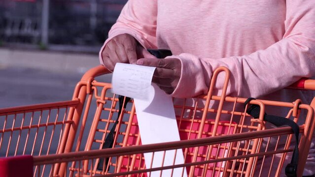 Woman checks paper receipt near shopping grocery store supermarket. Customer or buyer read food prices on bill. Food costs inflation due crises and unstable economy. Expensive grocery and budget.