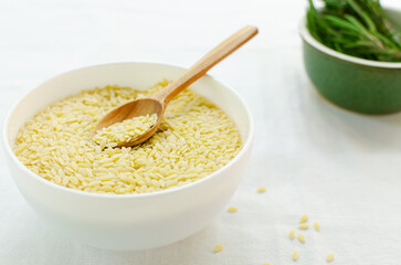 Raw risoni pasta with a sprig of rosemary with a wooden spoon on a light background. The concept of traditional Italian cuisine. Horizontal orientation. copy space.
