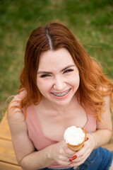 Top view of young beautiful red-haired woman smiling with braces and going to eat ice cream cone outdoors in summer